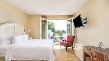 Habitación de hotel con cama, escritorio, silla, televisor y balcón con vistas.