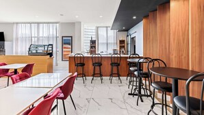 Un café moderne avec un sol en marbre, des chaises rouges et noires, un comptoir en bois et un espace bar.