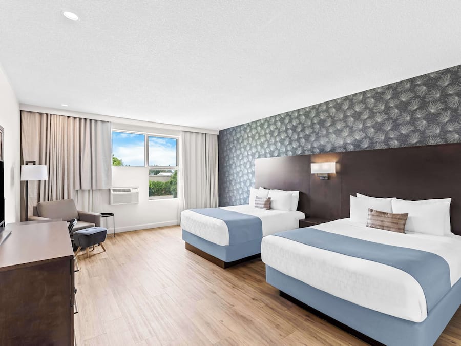 Ein Hotelzimmer mit zwei Betten, einem Schreibtisch, einem Fernseher und einem Fenster mit Vorhängen.