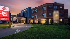 Un hôtel doté d’une façade moderne en briques, d’un grand réservoir d’eau cylindrique et d’une enseigne publicitaire indiquant les services offerts par « Best Western PLUS ».