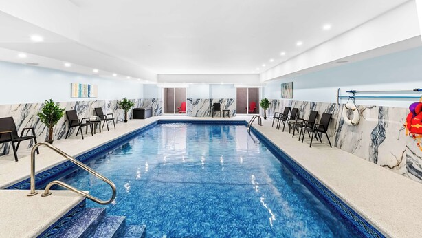 Une piscine avec un mur en marbre et des marches menant à l’eau. On y trouve des chaises, dont une chaise rouge, près de la piscine.