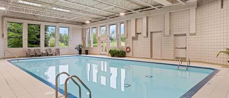 An indoor swimming pool with clear blue water, surrounded by tiled walls and large windows.