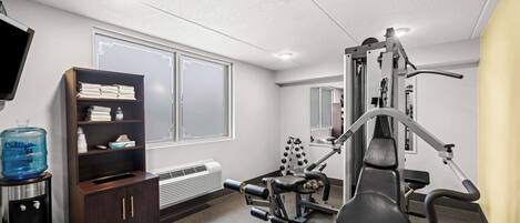 A gym with exercise equipment, a water dispenser, a shelf with towels, and a large window.