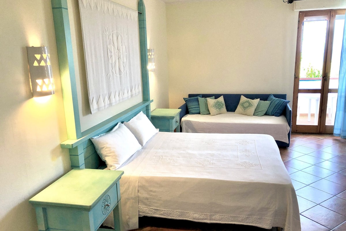 A room with two beds, a nightstand, a wall-mounted light fixture, and a sliding glass door leading to an outdoor area.