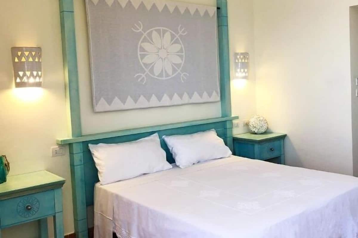 A bedroom with a bed, two bedside tables, a wall-mounted decorative piece, and two wall-mounted light fixtures.