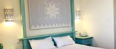 Un dormitorio con una cama, dos mesitas de noche, un adorno en la pared y dos lámparas fijadas a la pared.