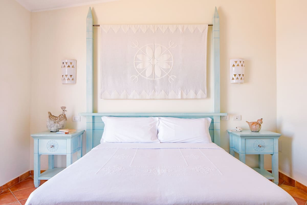 A bedroom with a large bed, two nightstands, and a decorative wall hanging.