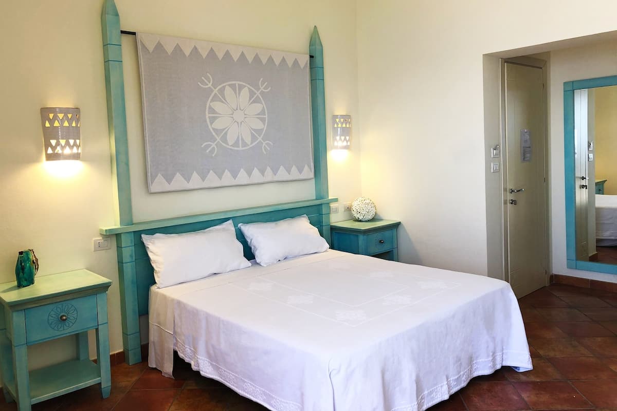 A bedroom with a bed, two nightstands, a wall-mounted light fixture, and a door.