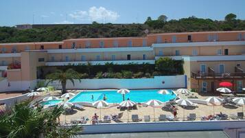 Un hotel con piscina rodeada de tumbonas y sombrillas, zona de playa y vistas a una colina.
