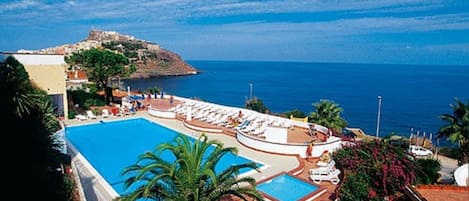 Un resort con una piscina grande, tumbonas y vistas al mar y a una colina.