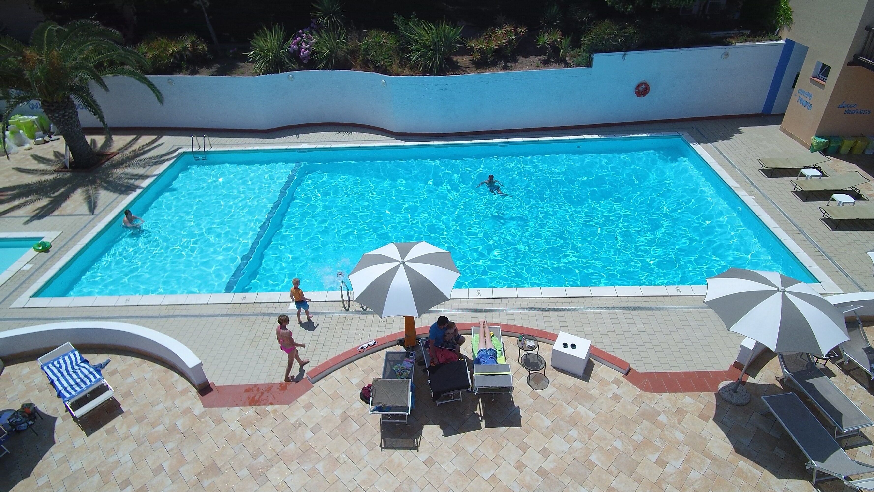 Una piscina rettangolare con bordo piastrellato, sdraio e ombrelloni.