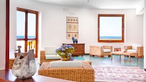 A spacious living room with wicker furniture, a large window with a view, and a decorative vase on a wooden table. - LH Pedraladda Resort (Castelsardo)
