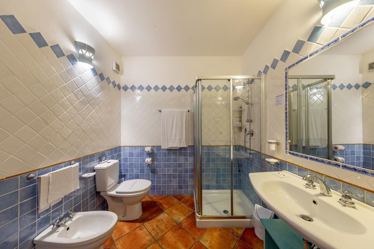 A bathroom with a glass-enclosed shower, a sink, a bidet, and a toilet.