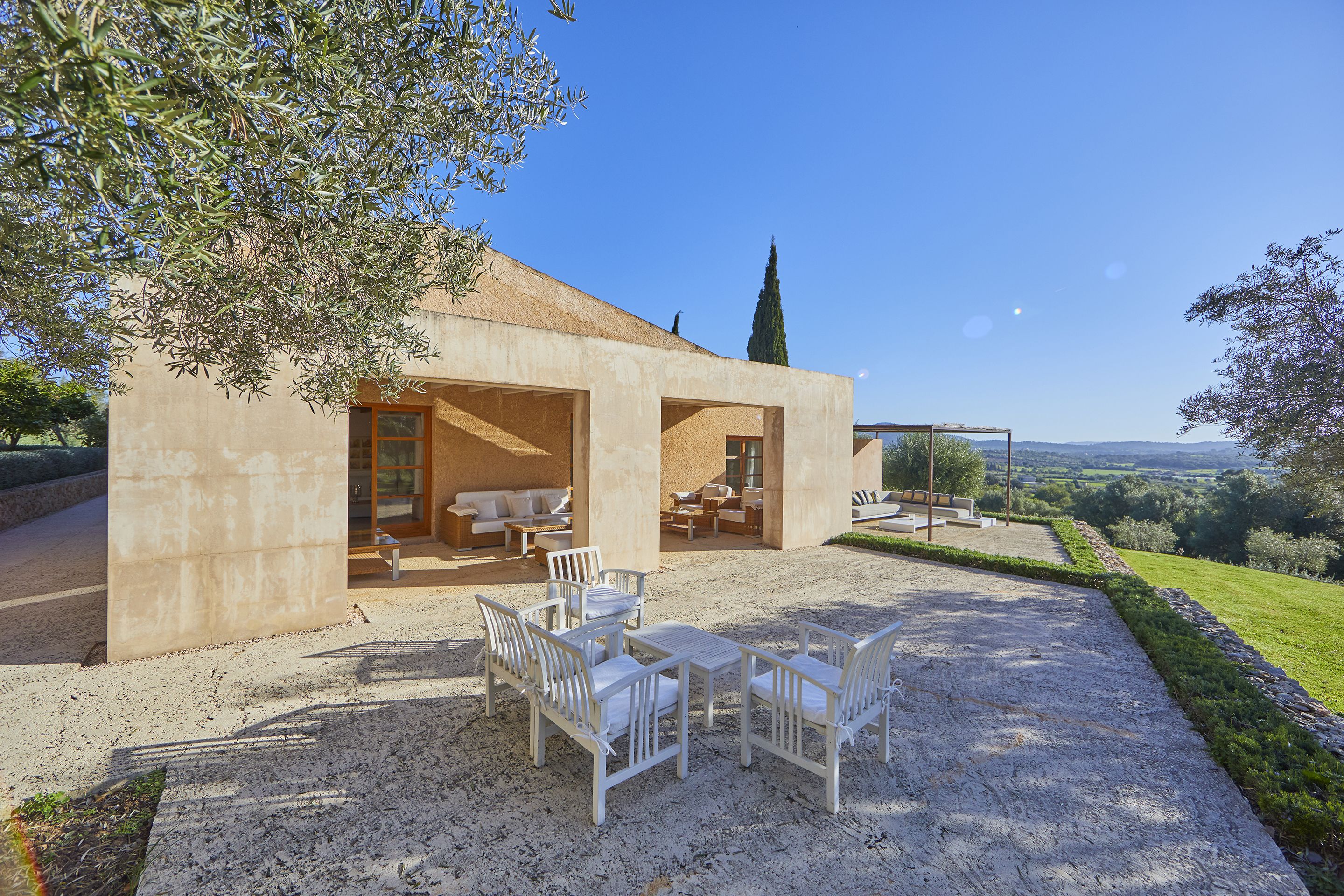 A modern outdoor patio with white furniture, a stone pathway, and a view of the countryside.