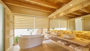 Une salle de bain moderne avec une baignoire sur pieds, un mur d’accent en pierre et un plafond en bois.