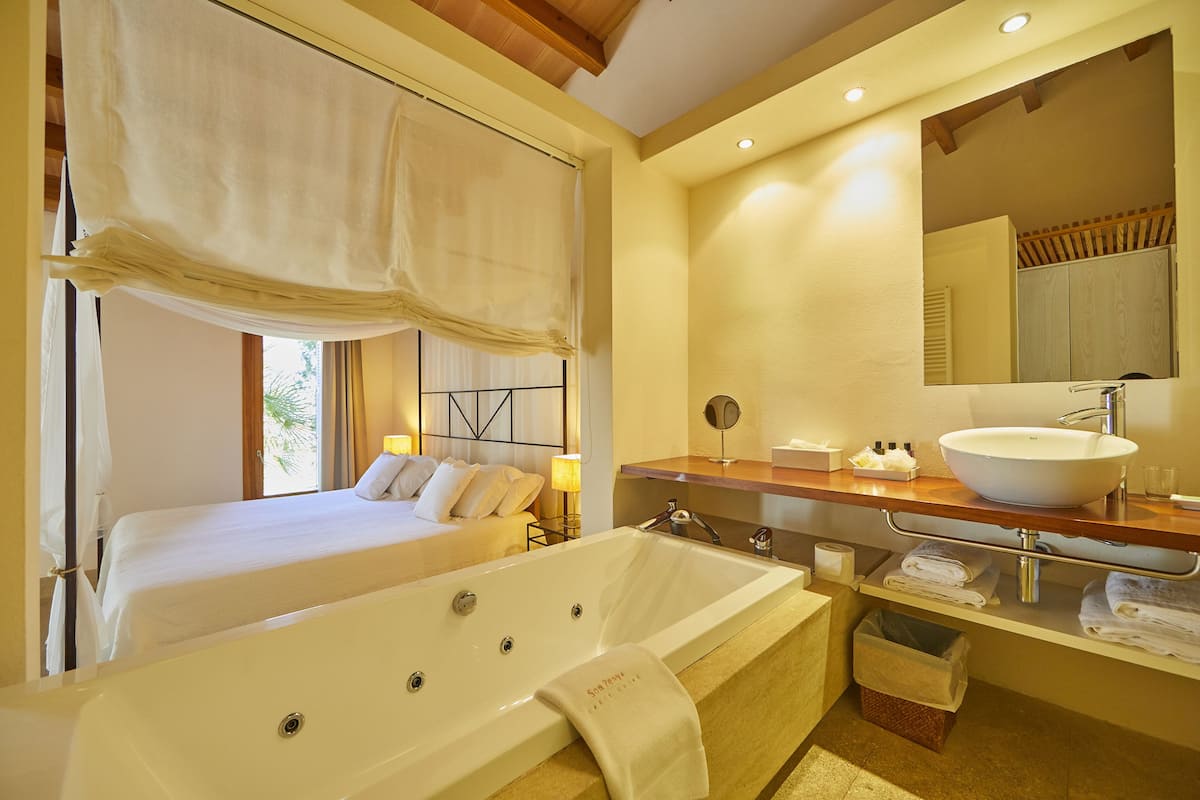 Une chambre d’hôtel dotée d’un grand lit, d’une salle de bain séparée avec une baignoire, et d’une coiffeuse avec un lavabo et un miroir.