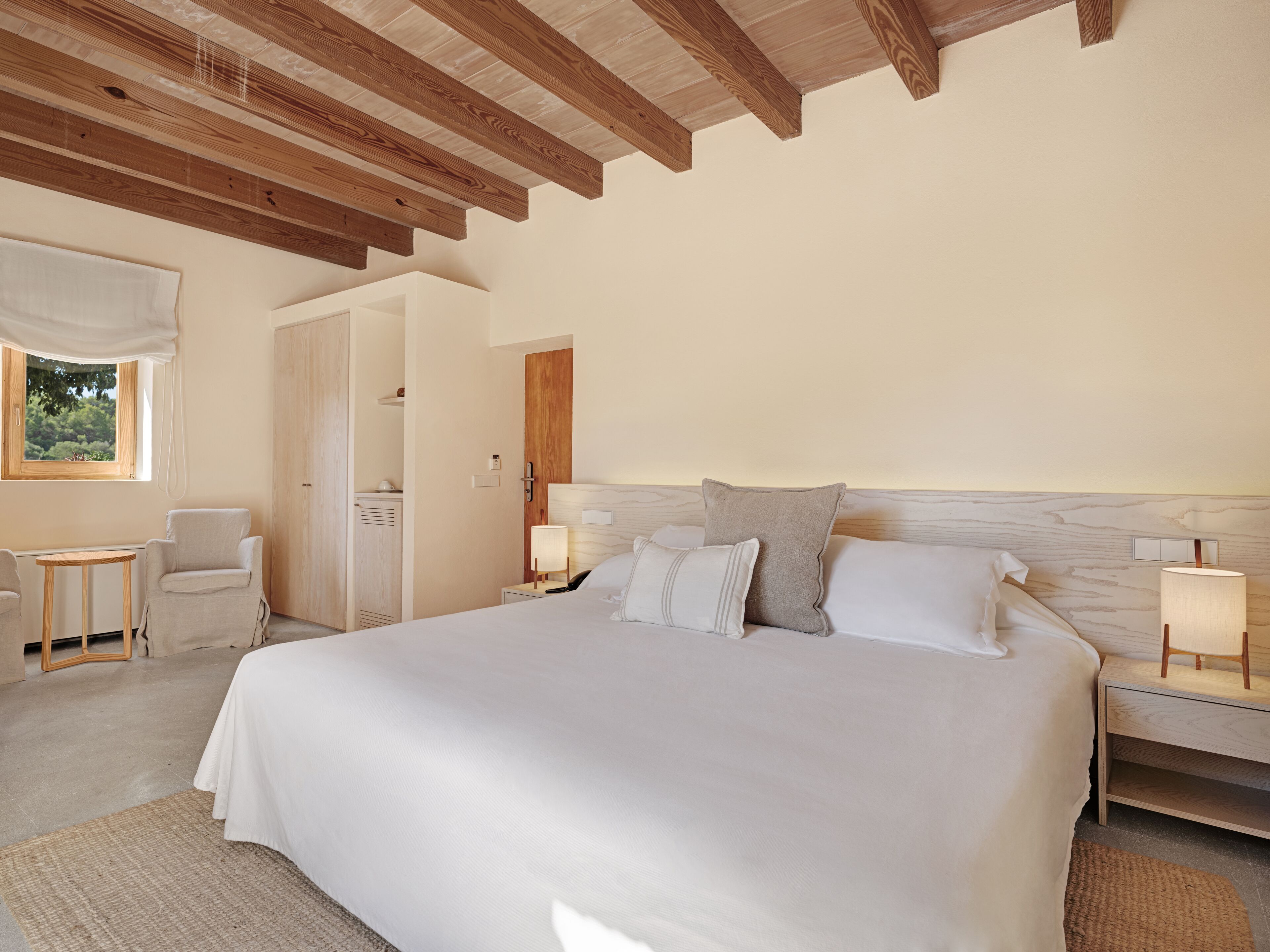 Un dormitorio amplio con una cama grande, techo de madera, una mesita y una silla.