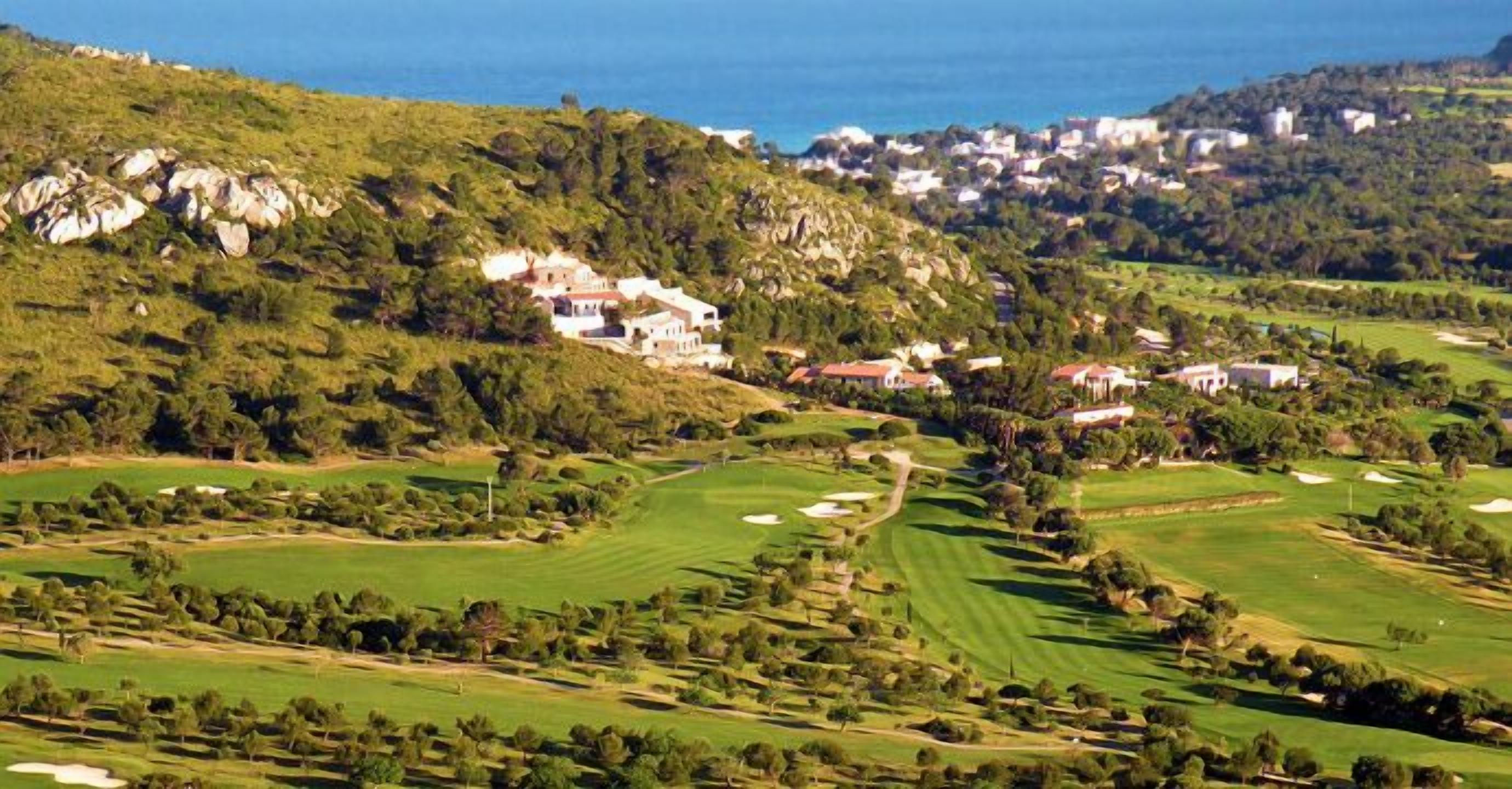 A golf course with multiple bunkers, a clubhouse, and a view of the sea.