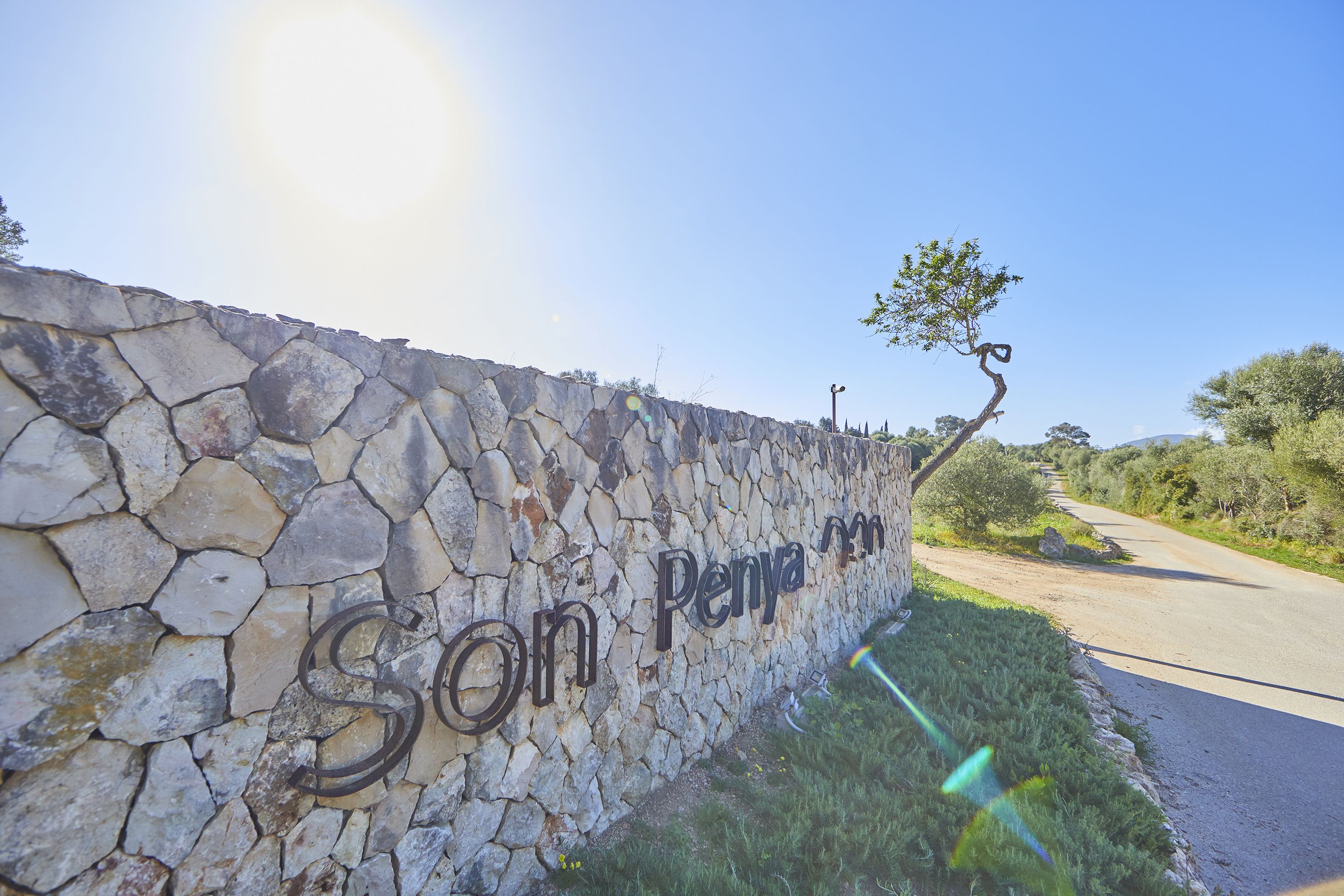 Un muro de piedra con la inscripción "Son Penya" y un camino estrecho a su lado.