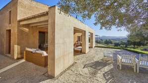 Un bâtiment moderne à l’extérieur en béton, doté d’un espace extérieur aménagé avec des coussins blancs et offrant une vue sur le paysage.