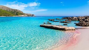Une plage côtière aux eaux turquoise et limpides, bordée de formations rocheuses et d’un rivage sablonneux.