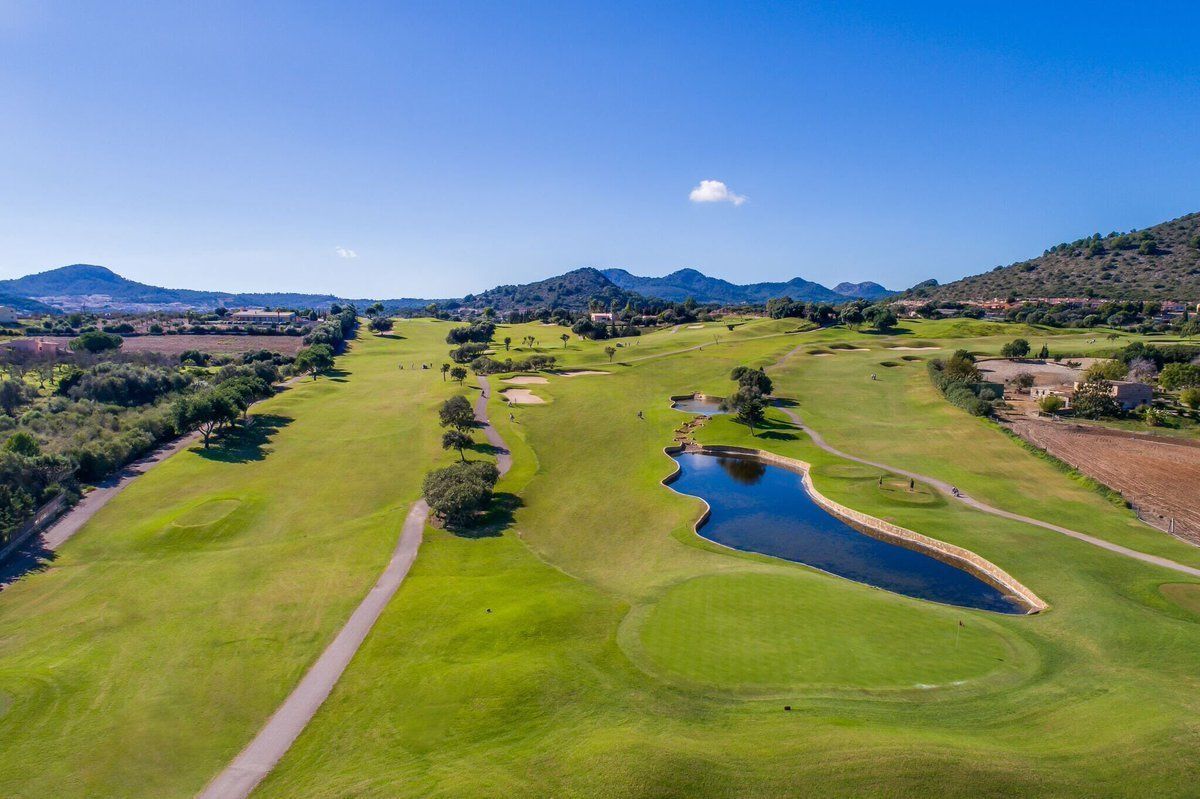 Vue aérienne d’un terrain de golf avec un étang, des allées et des montagnes au loin.