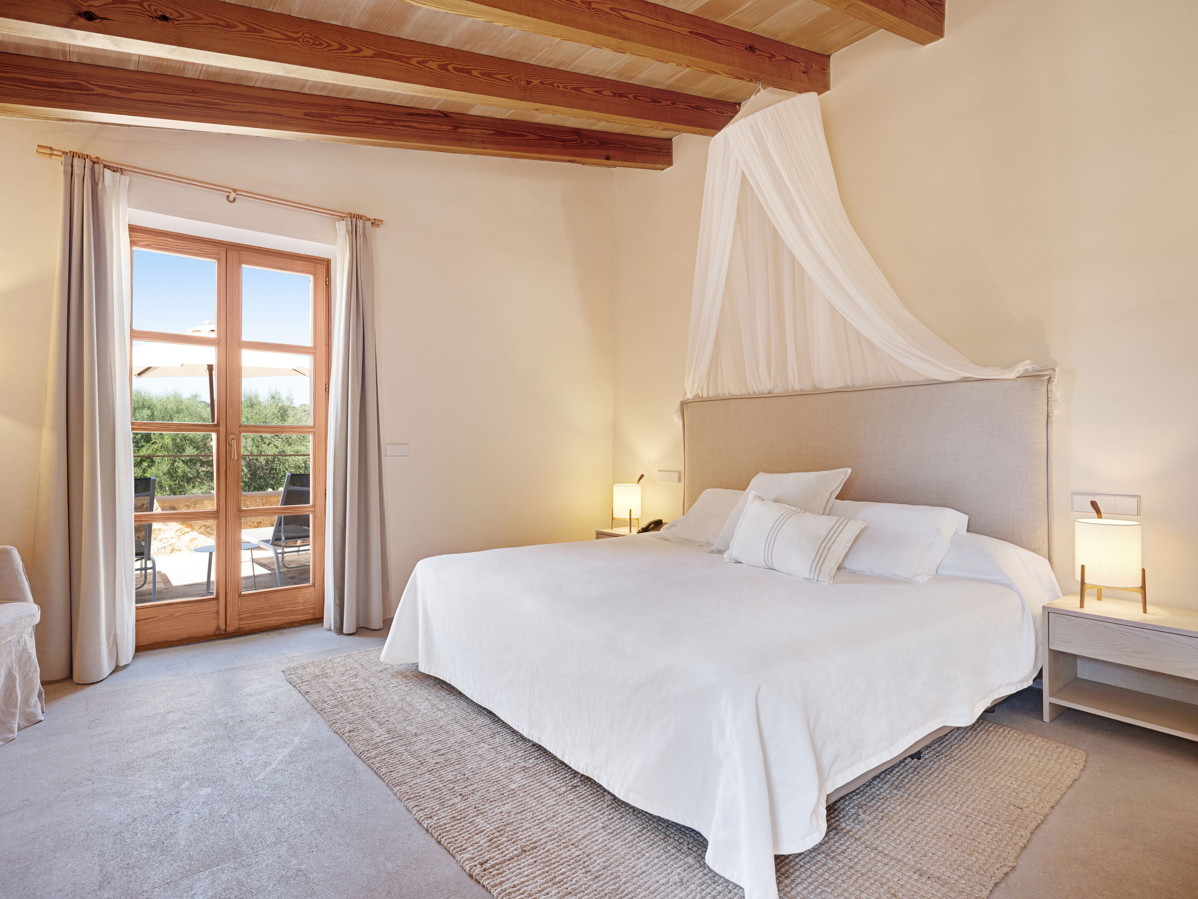A bedroom with a large bed, a canopy, a nightstand, a lamp, and a view of the outdoors through a glass door.