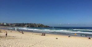 A beach with people, waves, and buildings in the background. - Ultimate Apartments Bondi Beach (Bondi Beach)