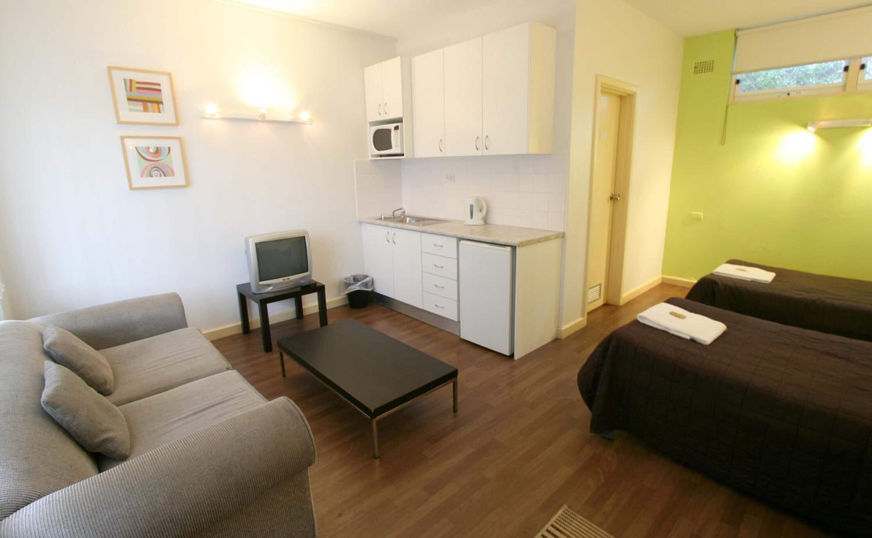 A compact living space with a kitchenette, a sofa, a small TV, and a bed.