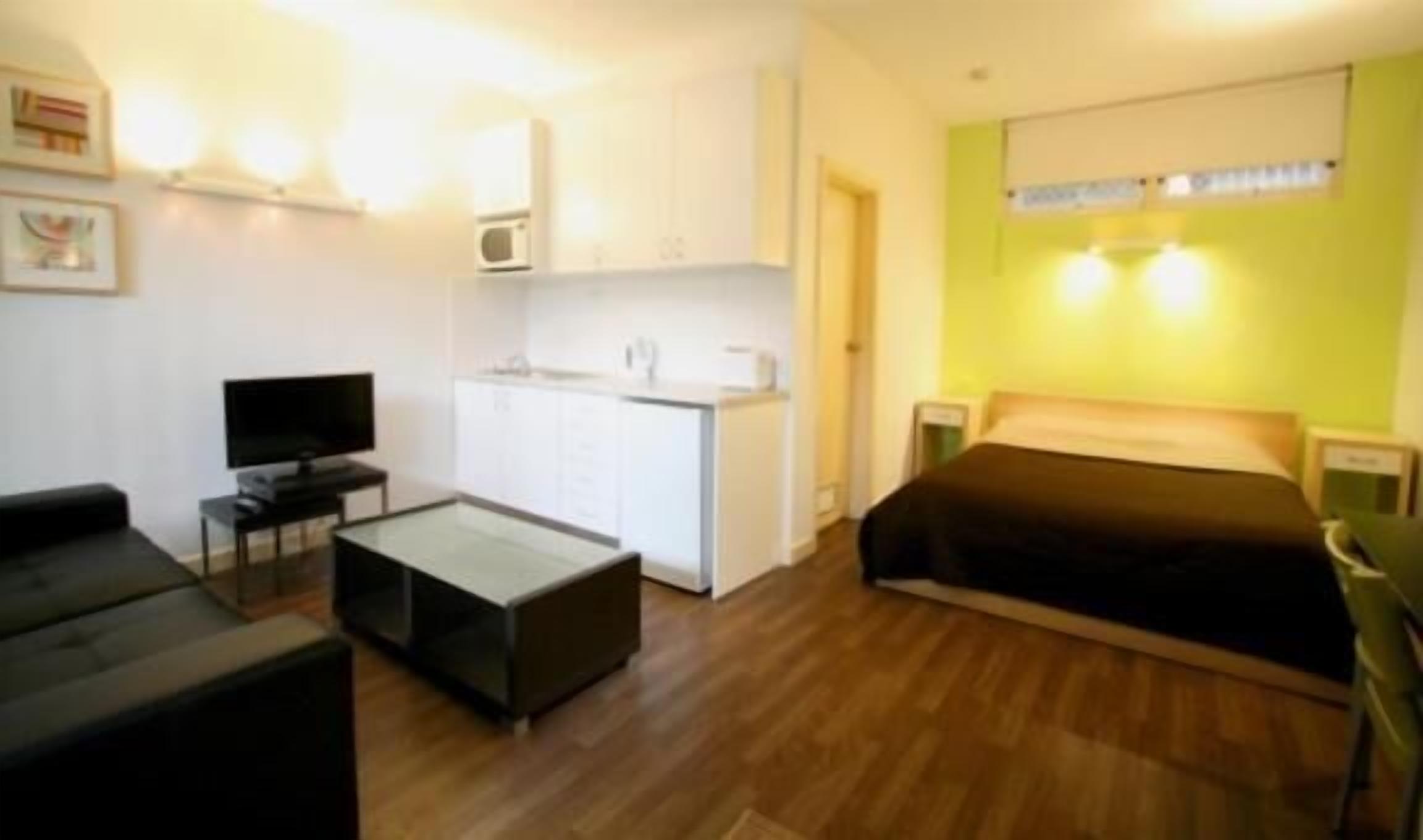Une chambre d’hôtel compacte comprenant un lit, une petite kitchenette, une télévision et un coin salon.