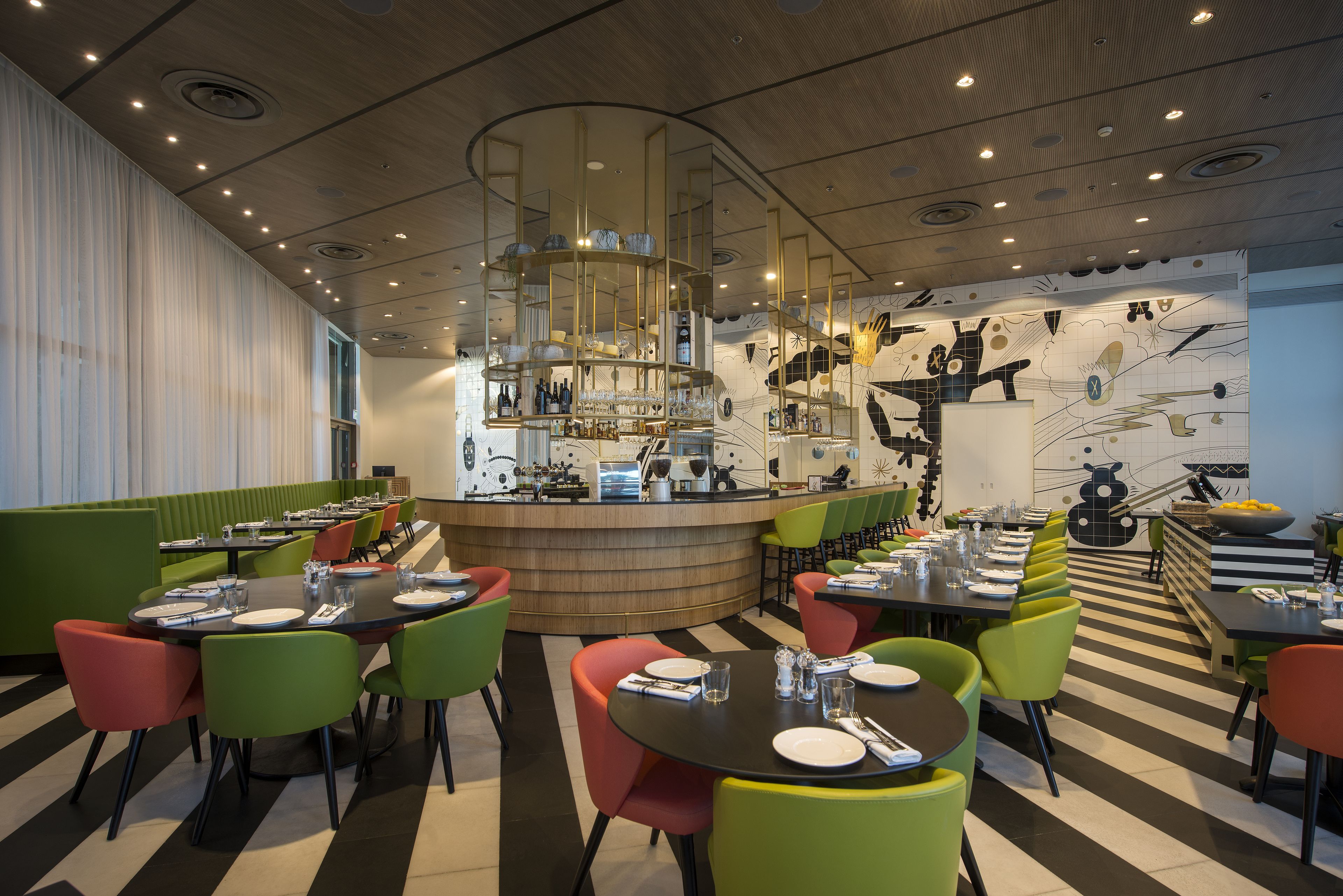 Un restaurante con una barra central, varias mesas de comedor con sillas y un mural distintivo en la pared.