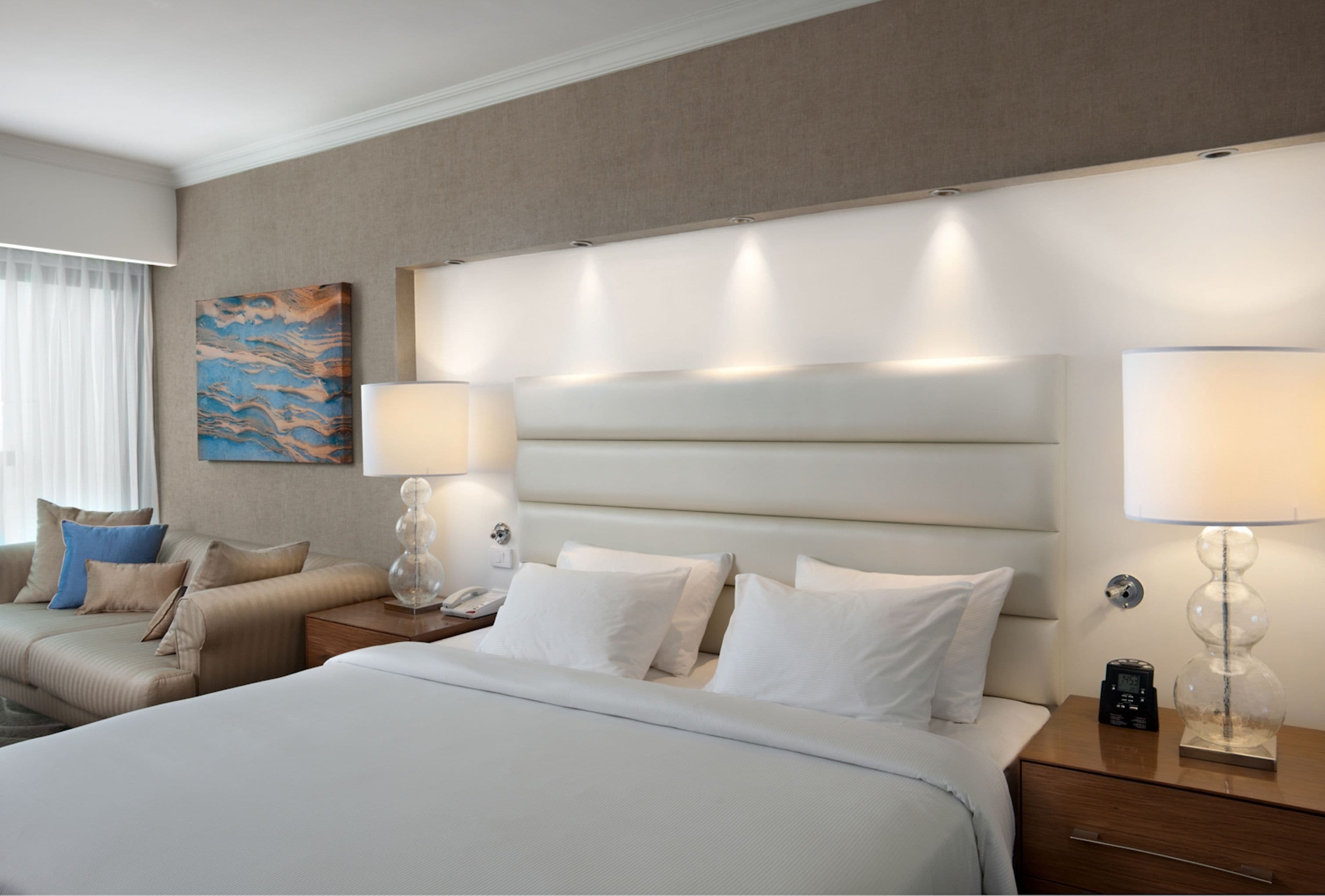 Una habitación de hotel con una cama grande, dos mesitas de noche, una lámpara de pared y un cuadro.