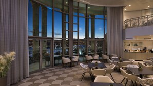 A modern hotel lobby with large windows, a patterned carpet, and a dining area with tables and chairs. - Queen of Sheba Eilat Hotel (Eilat)