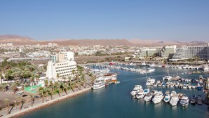 A marina with numerous boats docked, surrounded by a cityscape with buildings and palm trees. - Queen of Sheba Eilat Hotel (Eilat)