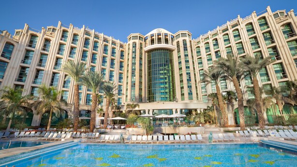 A large hotel with a central glass tower, a swimming pool with lounge chairs, and palm trees. - Queen of Sheba Eilat Hotel (Eilat)