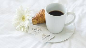A white cup of coffee, a croissant, and a white flower on a white surface.
