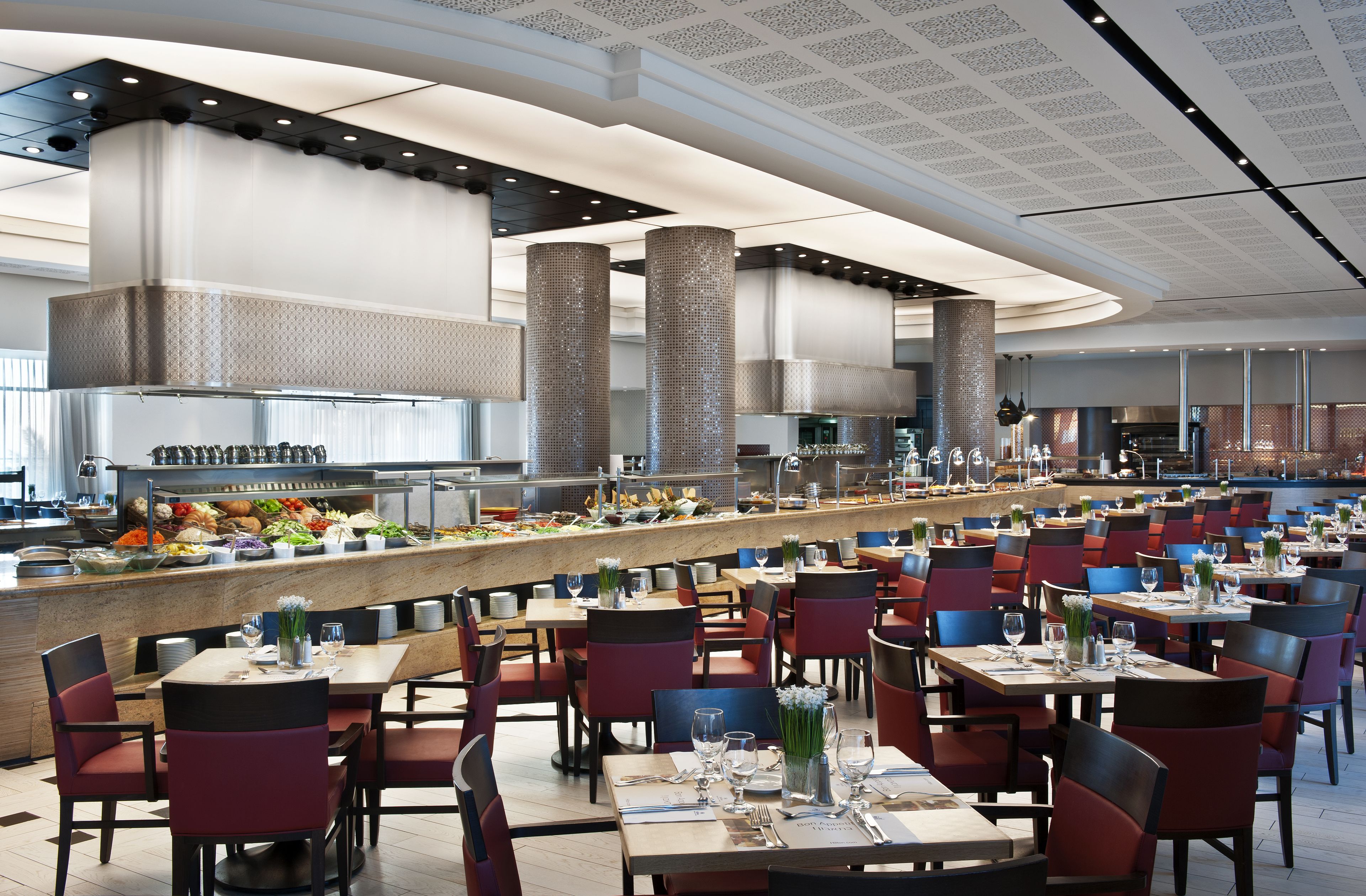 A spacious restaurant with high ceilings, a central bar area, and multiple dining tables and chairs.