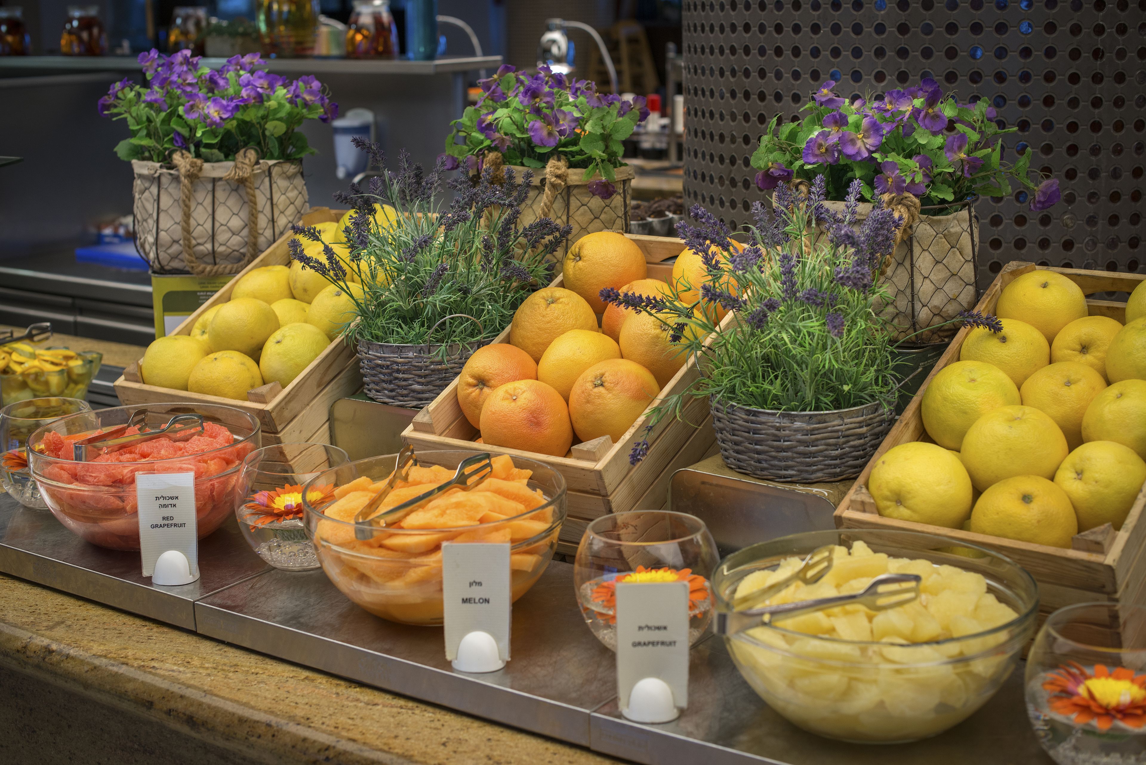 Ein Buffet mit verschiedenen Früchten und Gemüsesorten, darunter Zitronen, Orangen und Melonen, präsentiert in Holzkisten und Glasschalen.