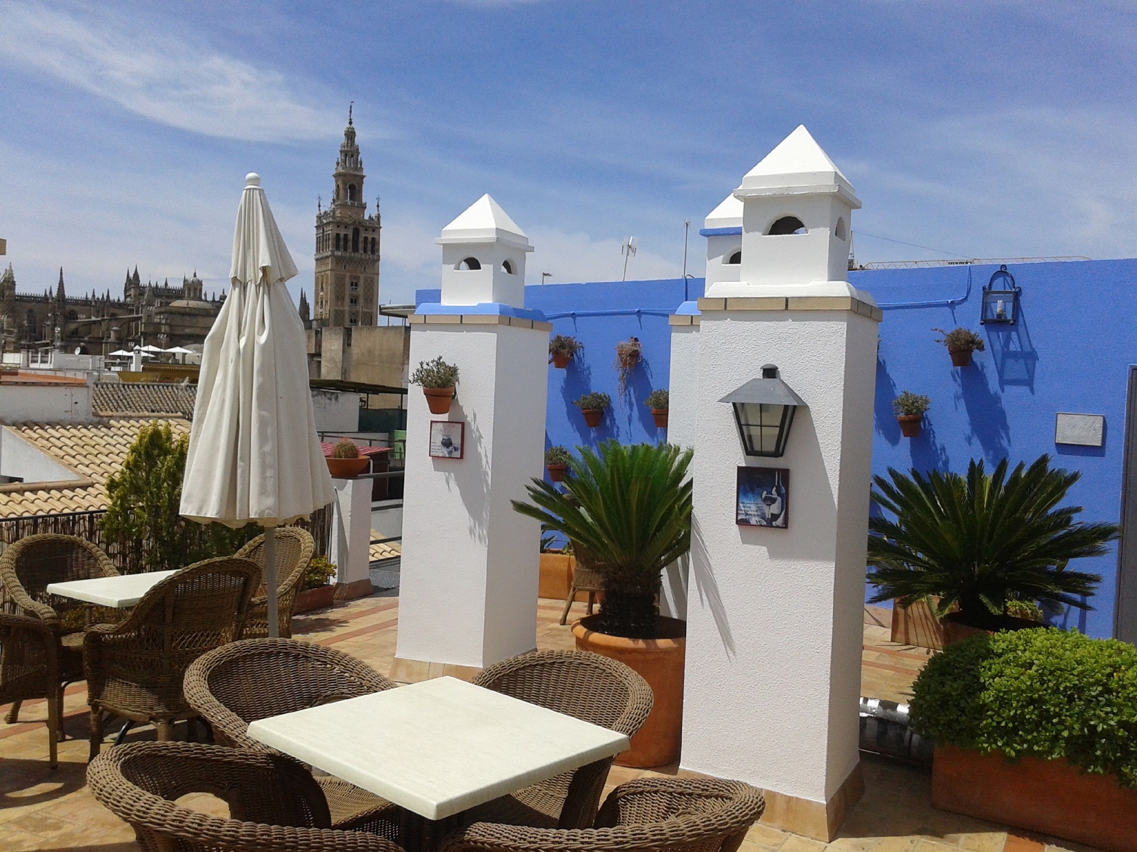 A rooftop patio with wicker furniture, potted plants, and a view of a historic tower.