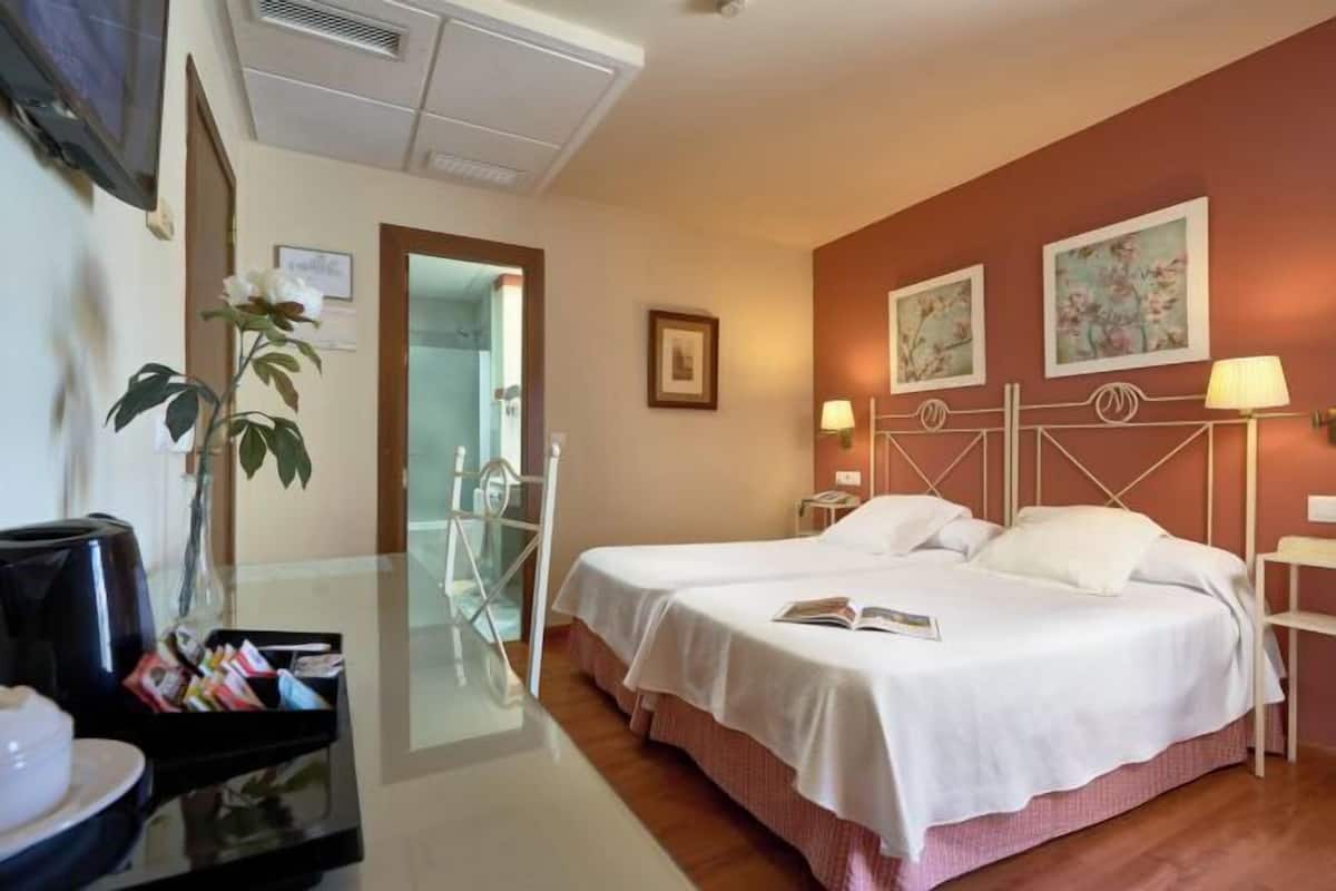 Une chambre d’hôtel avec deux lits, un bureau doté d’une machine à café, un miroir et des œuvres d’art accrochées aux murs.