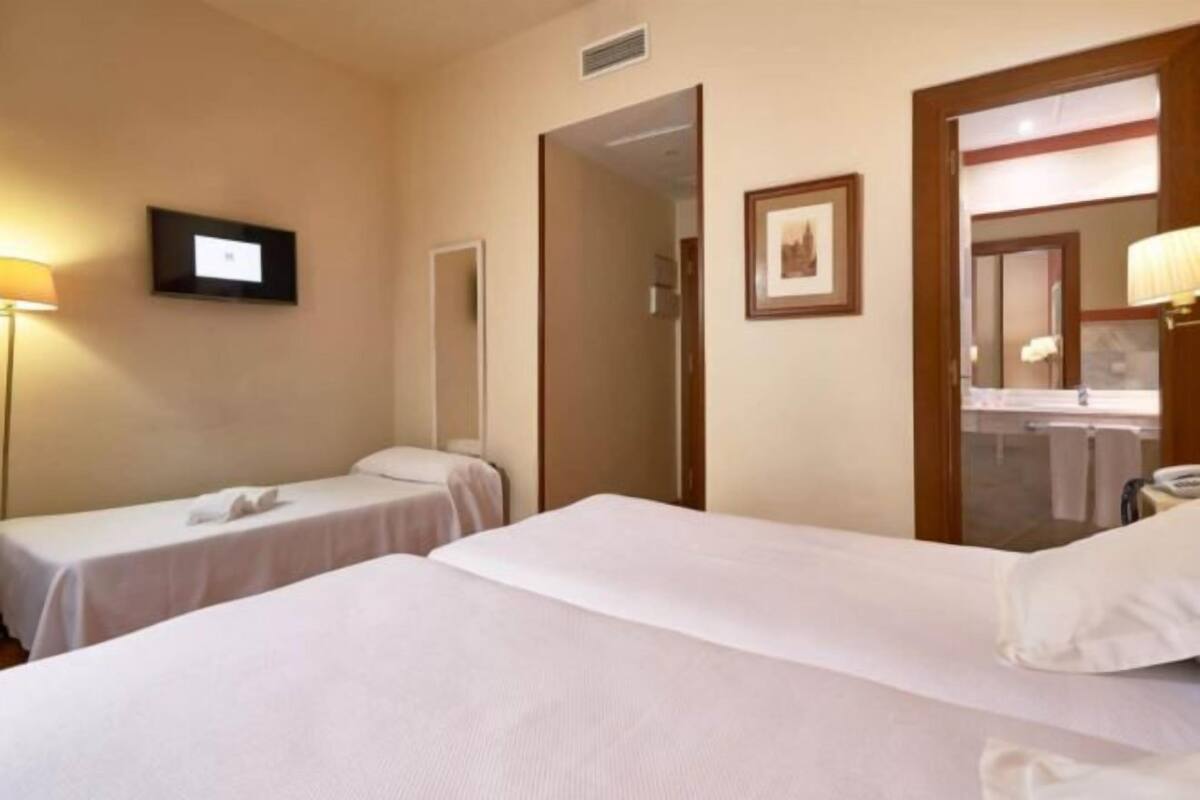 Une chambre d’hôtel avec deux lits, une lampe de chevet, un tableau encadré et un miroir.