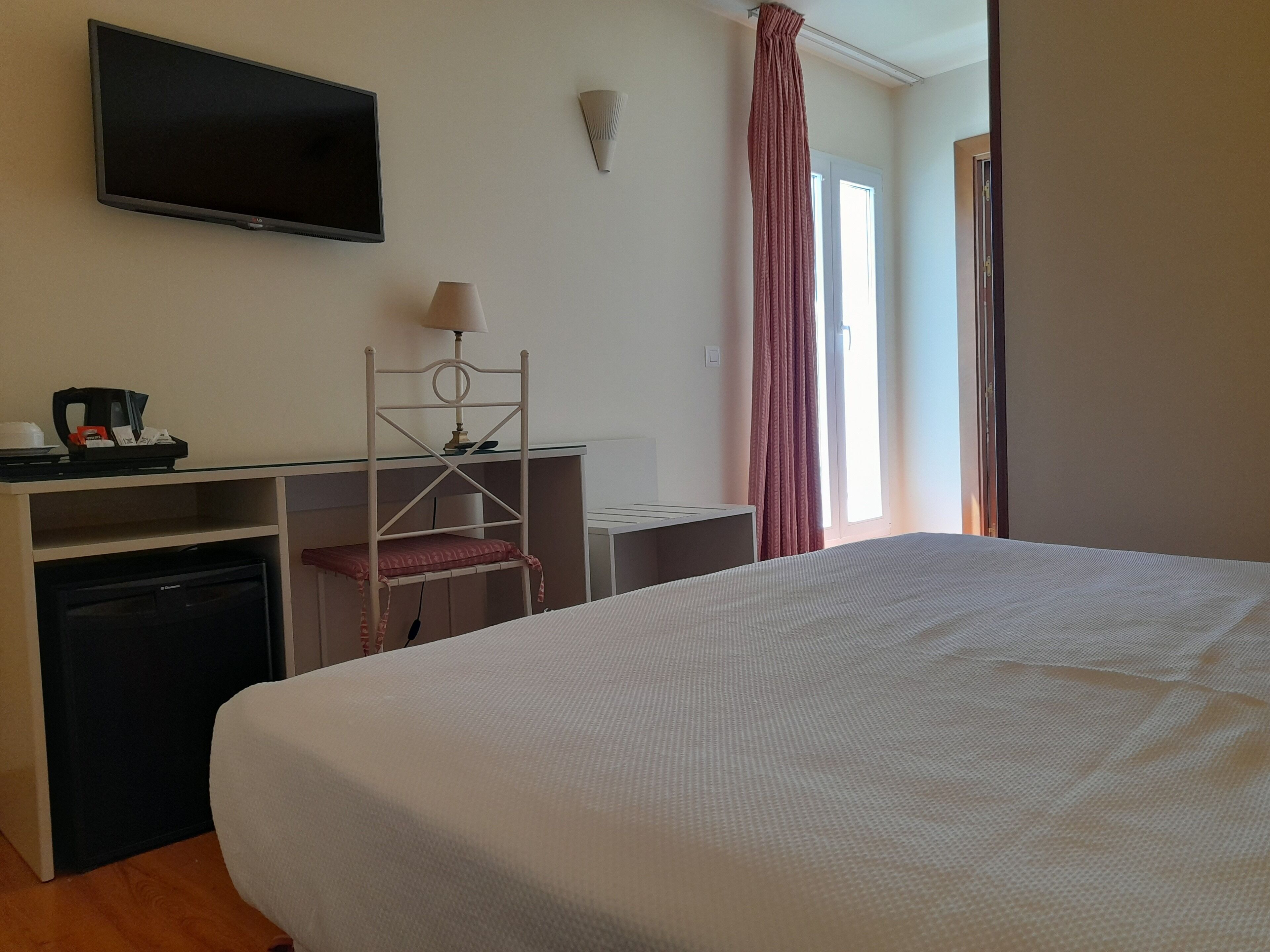 A hotel room with a bed, a desk with a computer, a TV, a lamp, and a window with curtains.