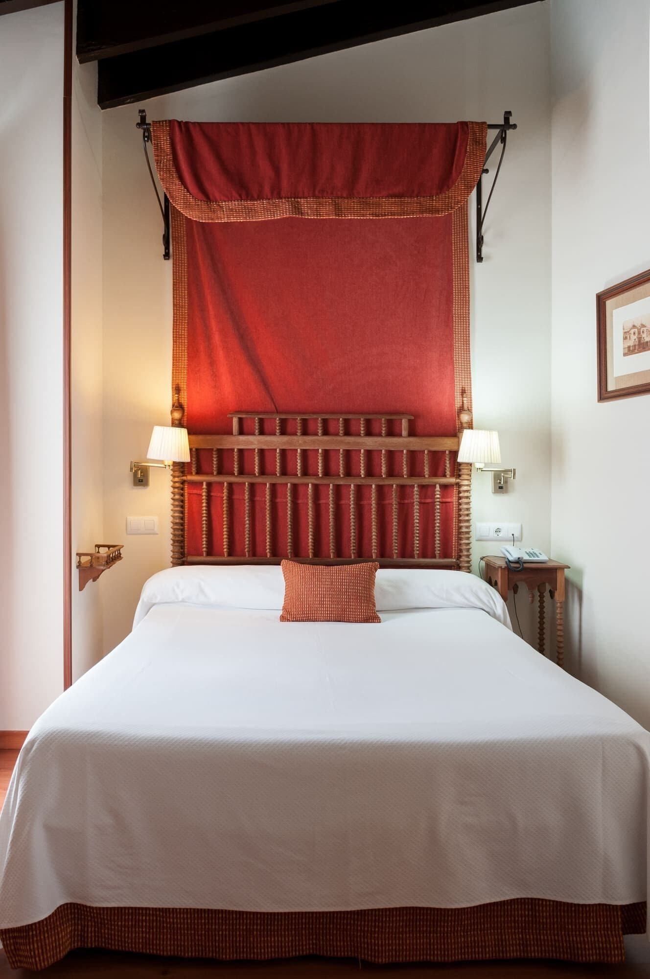 Ein Hotelzimmer mit einem großen Bett, einem roten Kopfteil, zwei Nachttischlampen und einem gerahmten Bild an der Wand.