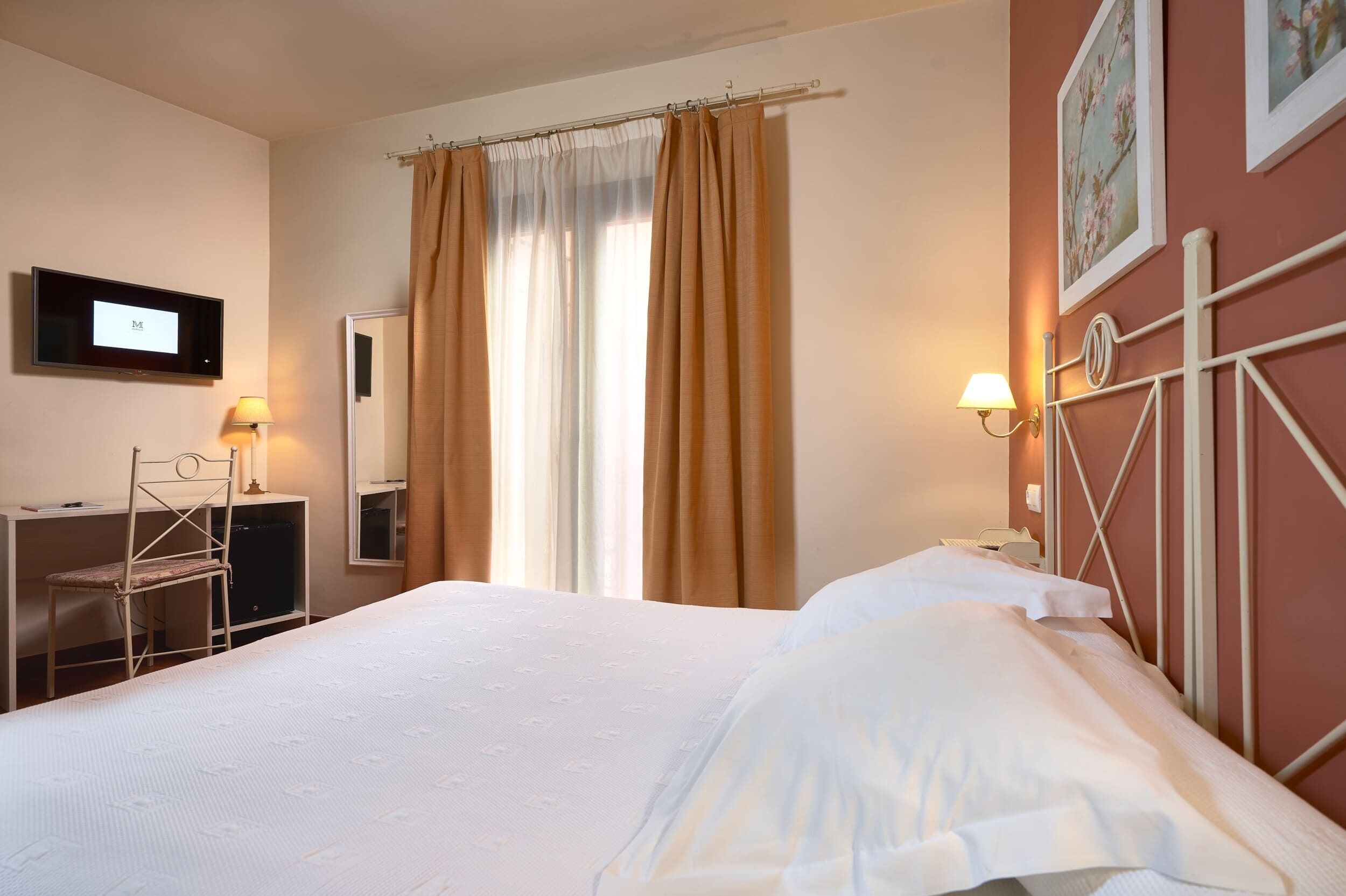 A hotel room with a bed, a desk, a chair, a TV, and curtains.