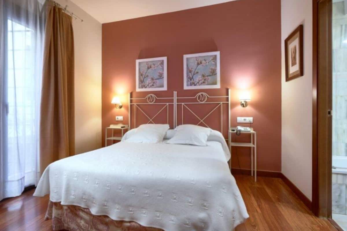 Une chambre d’hôtel avec un lit, deux lampes fixées au mur et deux tableaux encadrés accrochés au mur.