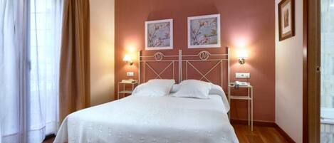 A hotel room with a bed, two wall-mounted lamps, and two framed pictures on the wall.