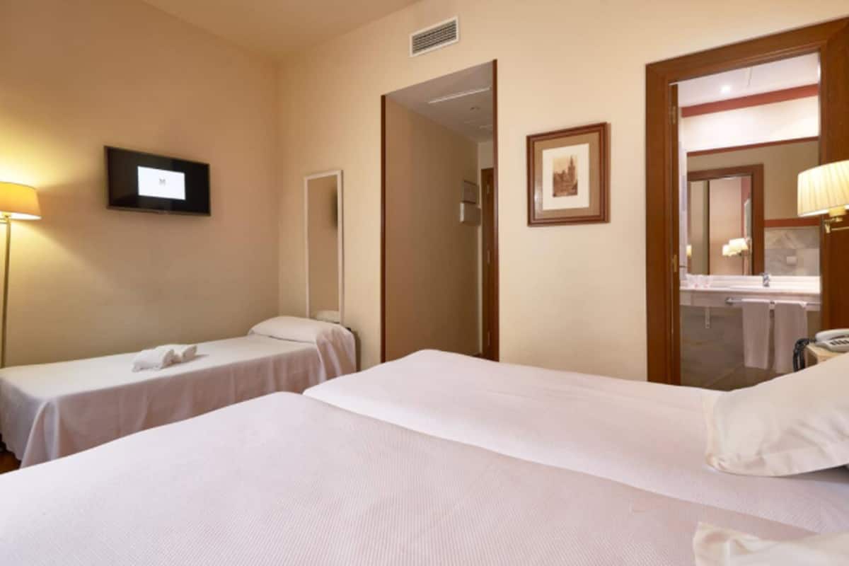 Une chambre d’hôtel avec deux lits simples, une télévision, un miroir et une salle de bain visible à travers une porte ouverte.