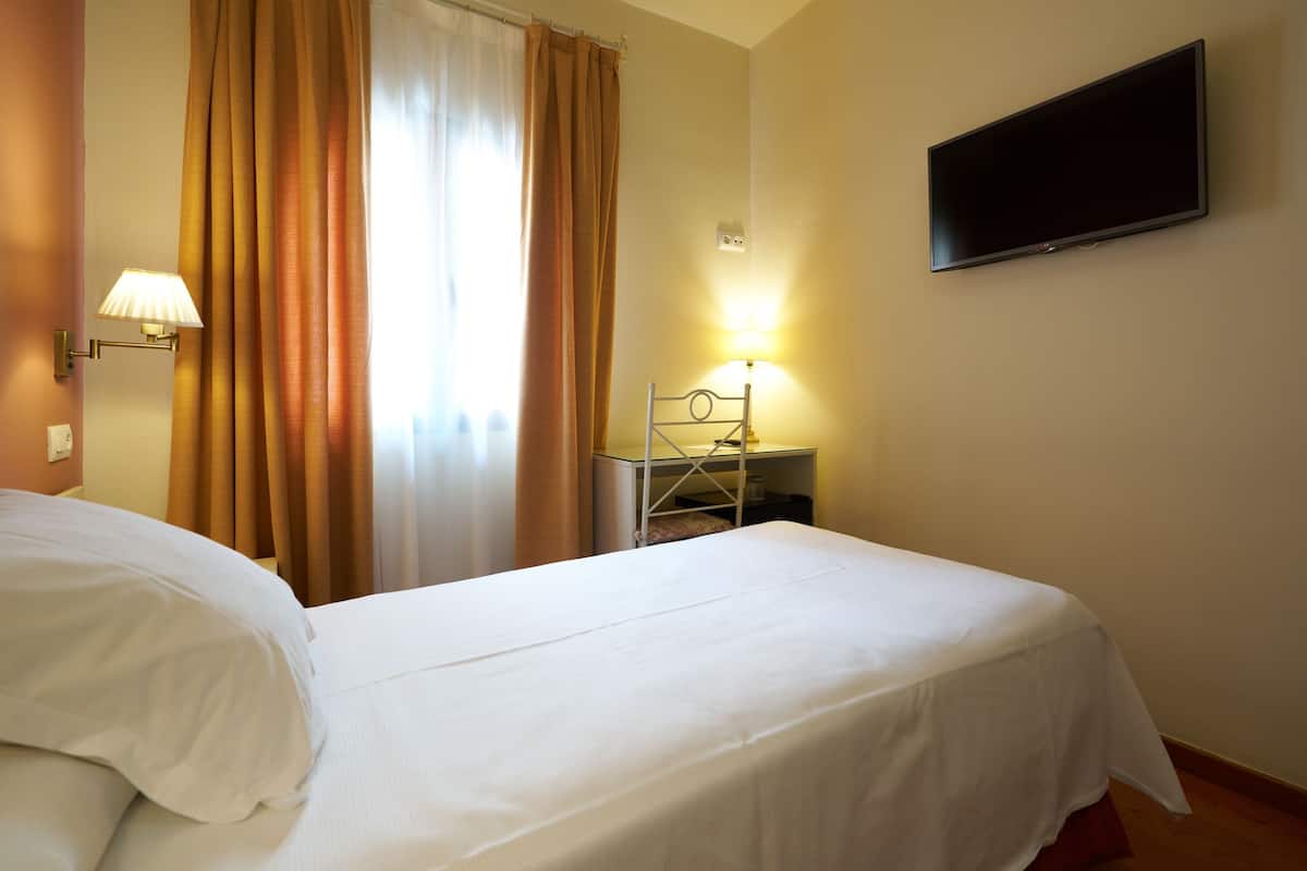 Une chambre d’hôtel avec deux lits, un téléviseur à écran plat, une lampe et une fenêtre avec des rideaux.