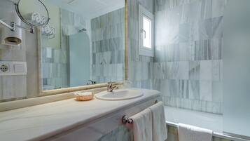 A bathroom with a marble wall, a sink with a mirror, and a towel hanging on the wall.