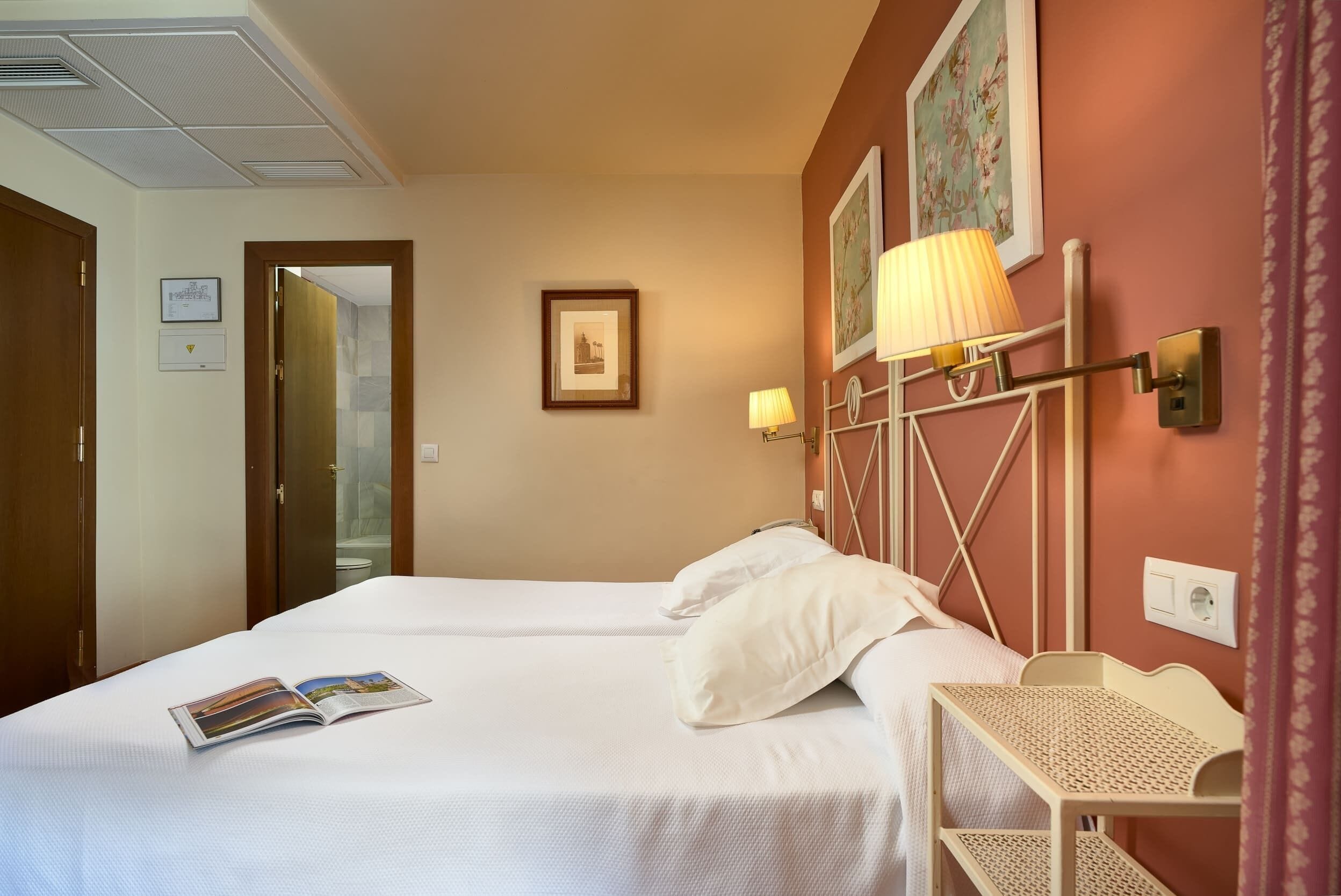 A hotel room with two beds, a small table, and a lamp.